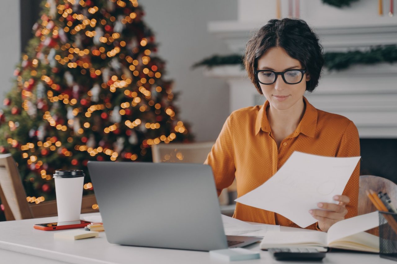 Female entrepreneur working online on laptop at Christmas in office with xmas tree in background